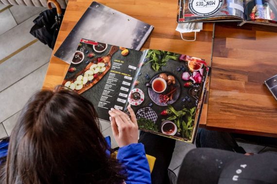 Two individuals explore food menus at a wooden table in a cozy café.