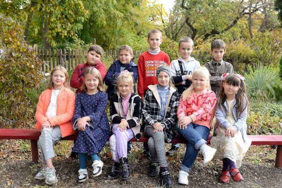 Happy group of kids sitting on a bench in a park during fall, enjoying a sunny day.